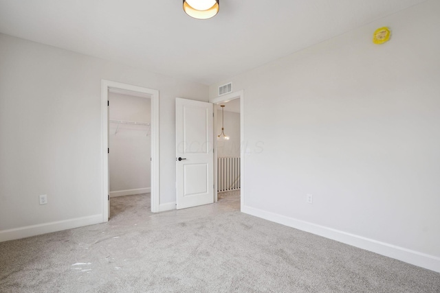 unfurnished bedroom with a walk in closet, carpet floors, visible vents, and baseboards