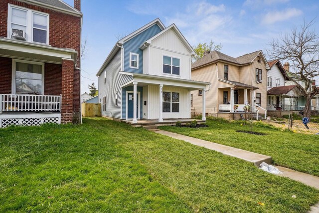 view of front of house featuring a front lawn, covered porch, fence, brick siding, and board and batten siding