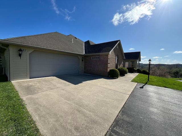 view of side of property featuring a yard, concrete driveway, a garage, and brick siding