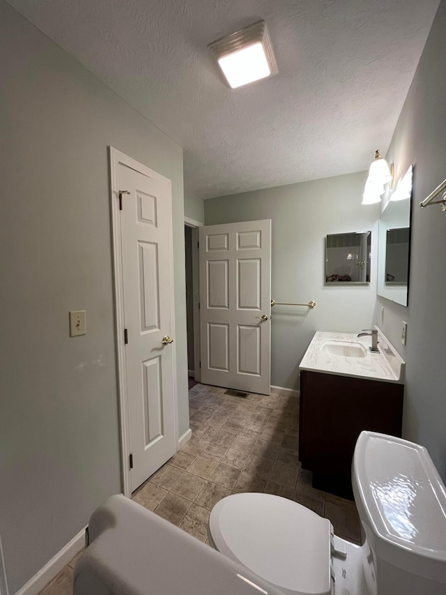 bathroom featuring vanity, baseboards, a textured ceiling, and toilet