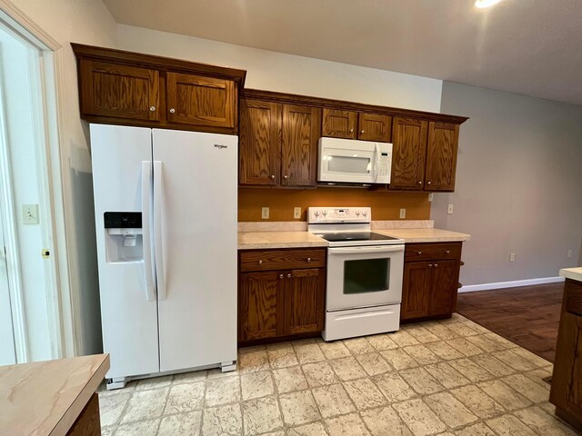 kitchen featuring light countertops, light floors, white appliances, and baseboards
