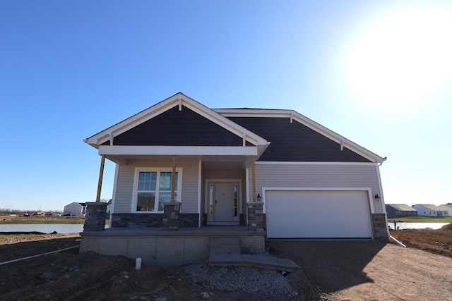 view of front of house featuring a water view, driveway, a porch, stone siding, and an attached garage