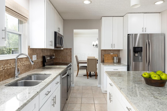 kitchen featuring appliances with stainless steel finishes, a sink, white cabinetry, tasteful backsplash, and light stone countertops