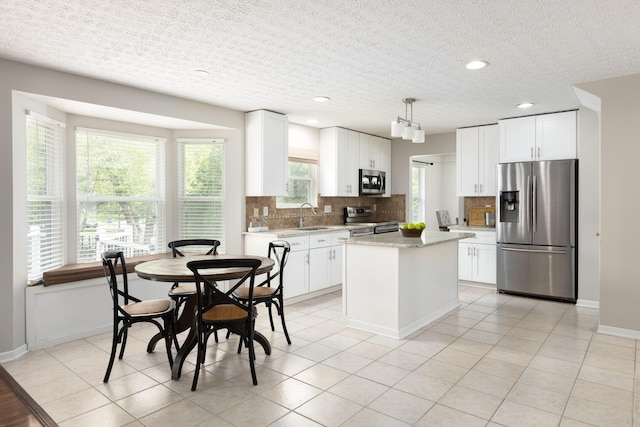 kitchen with stainless steel appliances, a sink, decorative backsplash, a textured ceiling, and a kitchen island