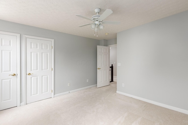 unfurnished bedroom featuring light colored carpet, baseboards, a textured ceiling, and ceiling fan