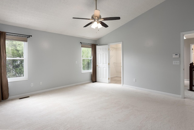 unfurnished bedroom featuring a spacious closet, light carpet, vaulted ceiling, multiple windows, and a textured ceiling