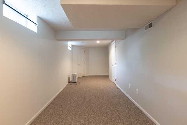 below grade area featuring a textured ceiling, carpet, and baseboards