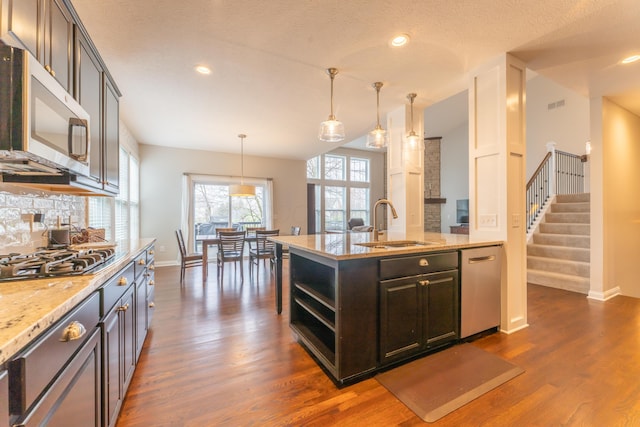 kitchen with tasteful backsplash, dark wood-style floors, light stone countertops, stainless steel appliances, and a sink