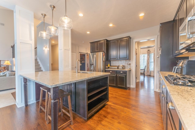 kitchen with appliances with stainless steel finishes, a breakfast bar, dark wood-style floors, decorative backsplash, and a sink