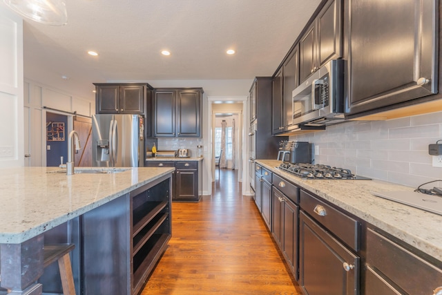 kitchen with light stone countertops, decorative backsplash, stainless steel appliances, a sink, and wood finished floors