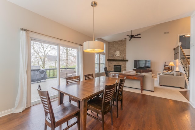 dining space with wood finished floors, a fireplace, vaulted ceiling, and stairs