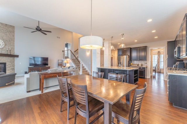 dining room featuring dark wood-style floors, a fireplace, a ceiling fan, and stairs