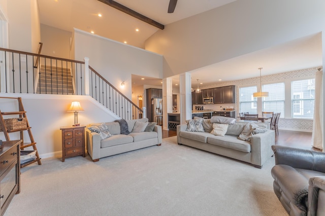 living area featuring baseboards, light carpet, stairway, beamed ceiling, and high vaulted ceiling