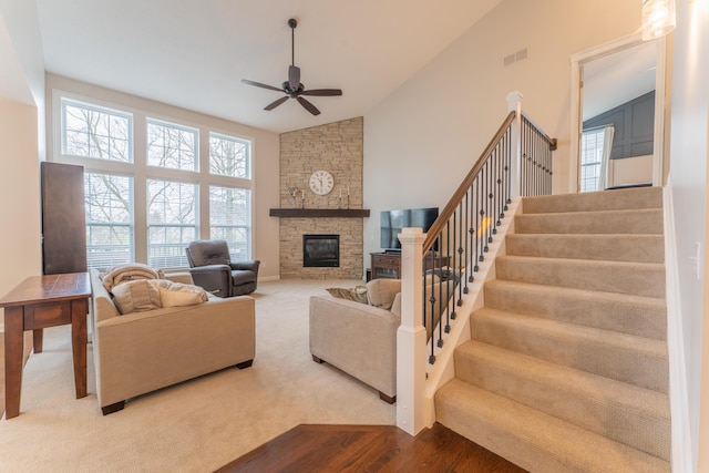living area with a fireplace, stairway, visible vents, ceiling fan, and high vaulted ceiling