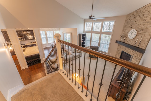 stairs with high vaulted ceiling, plenty of natural light, a stone fireplace, and ceiling fan