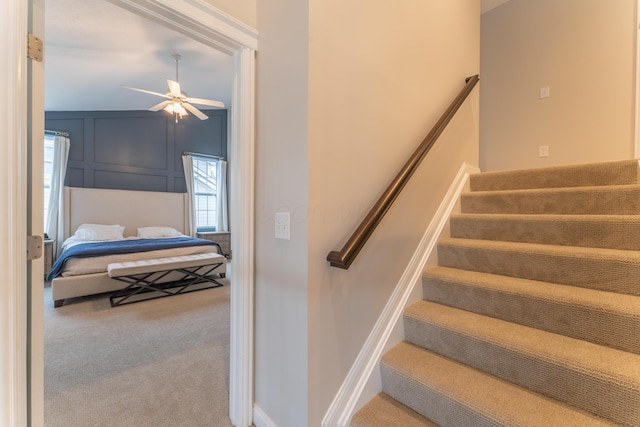 stairs with a decorative wall, baseboards, a ceiling fan, and carpet flooring