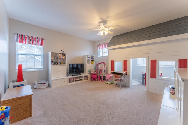 playroom with wooden walls, carpet floors, ceiling fan, and a healthy amount of sunlight