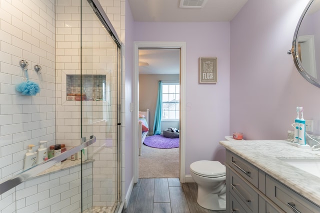 ensuite bathroom with toilet, a shower stall, vanity, and wood finished floors