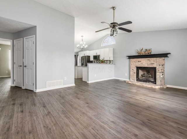 unfurnished living room with dark wood-style flooring, a brick fireplace, ceiling fan with notable chandelier, vaulted ceiling, and visible vents
