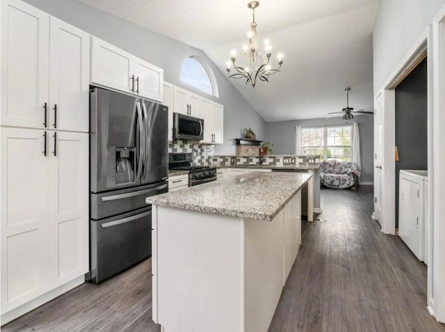 kitchen with appliances with stainless steel finishes, a center island, vaulted ceiling, a peninsula, and washer / dryer