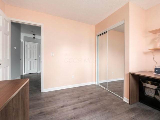 unfurnished bedroom with baseboards, a closet, and dark wood-type flooring