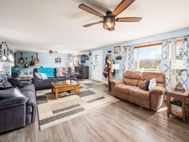living room with a wood stove, ceiling fan, and wood finished floors