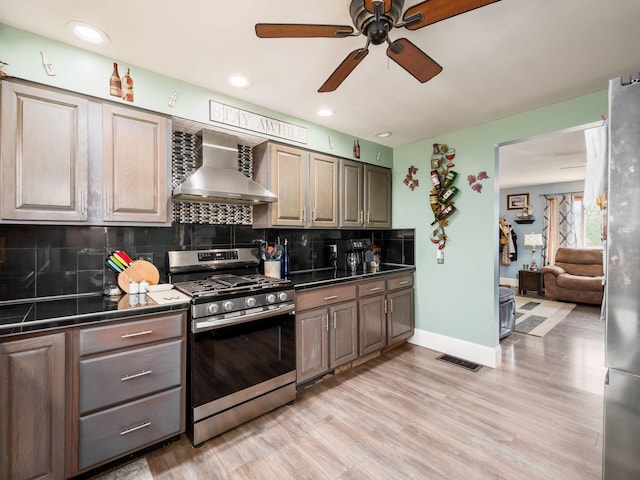 kitchen with ceiling fan, visible vents, wall chimney range hood, light wood-style floors, and stainless steel appliances