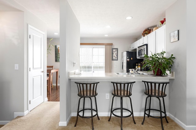kitchen featuring a breakfast bar, stainless steel microwave, refrigerator with ice dispenser, and white cabinetry