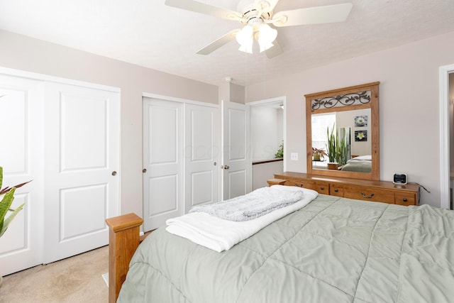 bedroom featuring light carpet, two closets, and ceiling fan