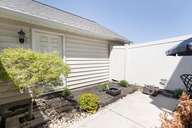 view of side of home featuring fence, a patio, and a shingled roof