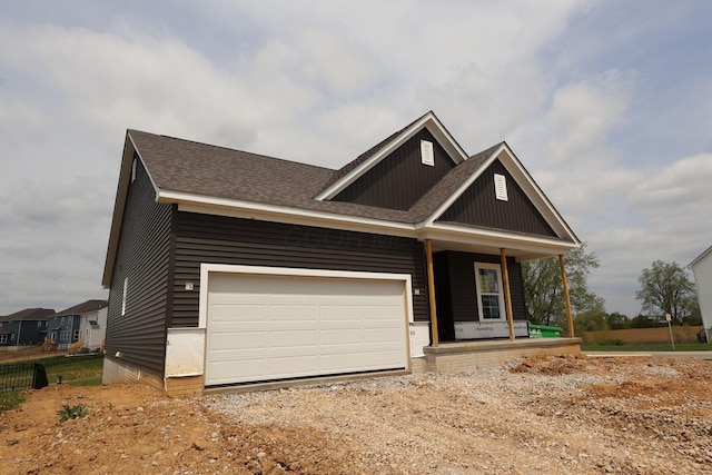 craftsman-style home with roof with shingles, an attached garage, board and batten siding, covered porch, and driveway