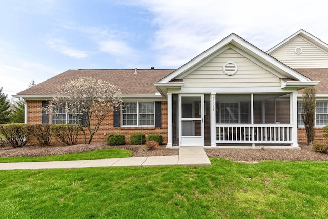 view of front facade featuring a shingled roof, a front lawn, and brick siding