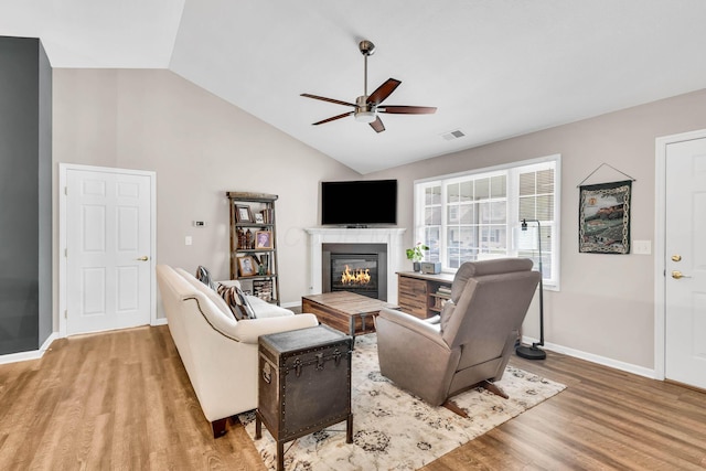living room featuring a glass covered fireplace, baseboards, light wood-style flooring, a ceiling fan, and visible vents