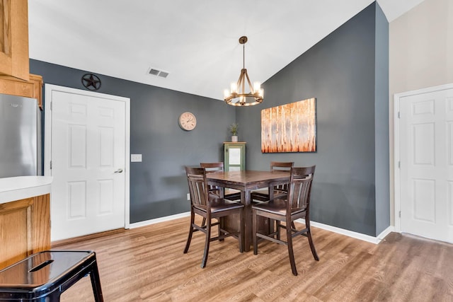 dining space featuring an inviting chandelier, visible vents, lofted ceiling, light wood finished floors, and baseboards