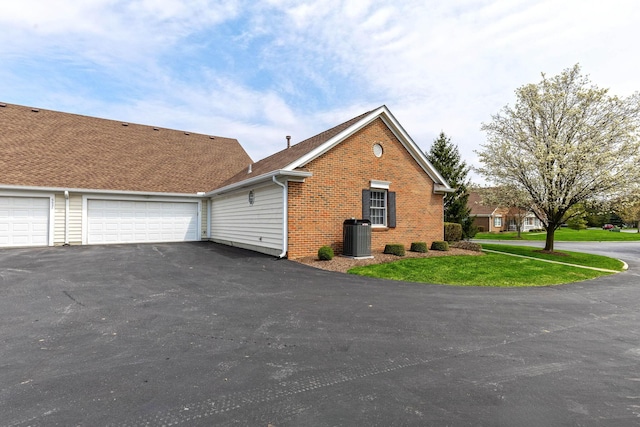 view of home's exterior featuring driveway, brick siding, central AC, a garage, and a yard
