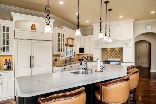 10577 Wellington Blvd, Powell, OH 43065 - kitchen featuring stove, arched walkways, a kitchen island with sink, a sink, and ornamental molding