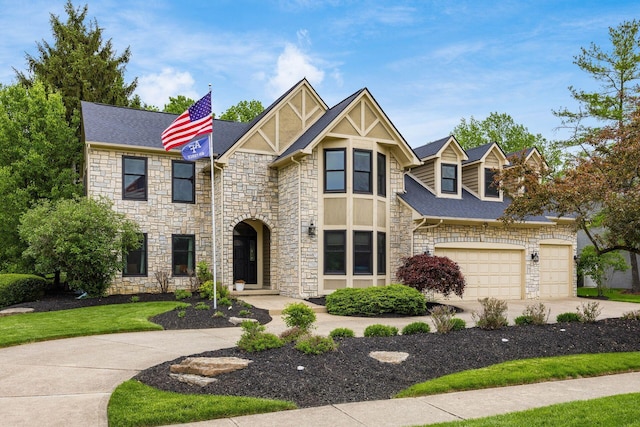 tudor-style house featuring stone siding, driveway, a garage, and roof with shingles