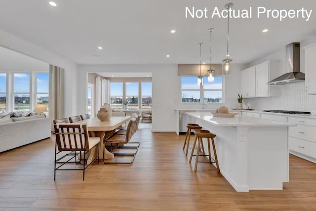 kitchen featuring a healthy amount of sunlight, a kitchen island, recessed lighting, and wall chimney range hood