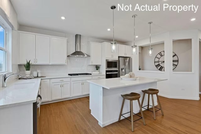 kitchen featuring a sink, black appliances, decorative backsplash, light countertops, and wall chimney exhaust hood