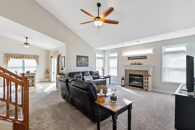 living area featuring high vaulted ceiling, ceiling fan, light carpet, a tiled fireplace, and baseboards
