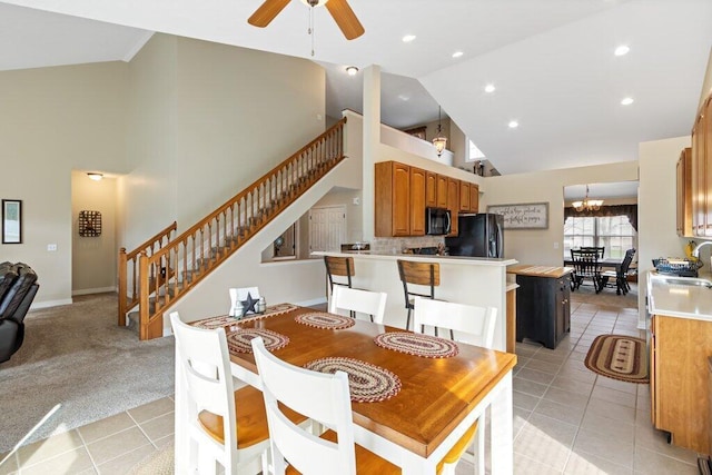 dining room with ceiling fan with notable chandelier, high vaulted ceiling, light tile patterned flooring, and stairs