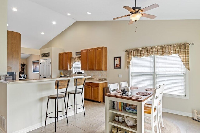 kitchen featuring light tile patterned floors, ceiling fan, brown cabinetry, a kitchen bar, and light countertops