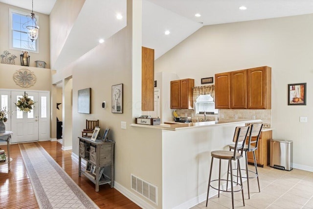 kitchen featuring high vaulted ceiling, brown cabinetry, visible vents, a breakfast bar, and light countertops