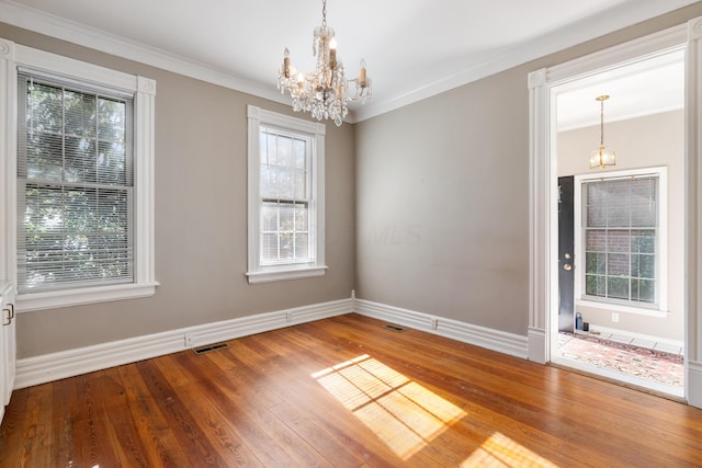 unfurnished room with a chandelier, baseboards, plenty of natural light, wood finished floors, and ornamental molding
