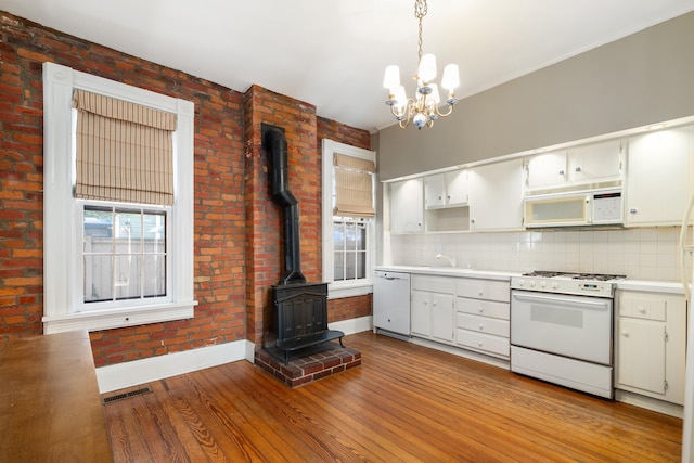 kitchen featuring white appliances, a wood stove, baseboards, wood finished floors, and a sink