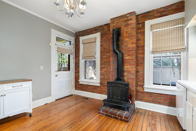 foyer with baseboards, a chandelier, a wood stove, light wood-style flooring, and ornamental molding
