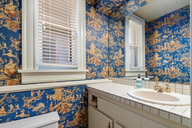 bathroom featuring healthy amount of natural light, vanity, toilet, and wallpapered walls
