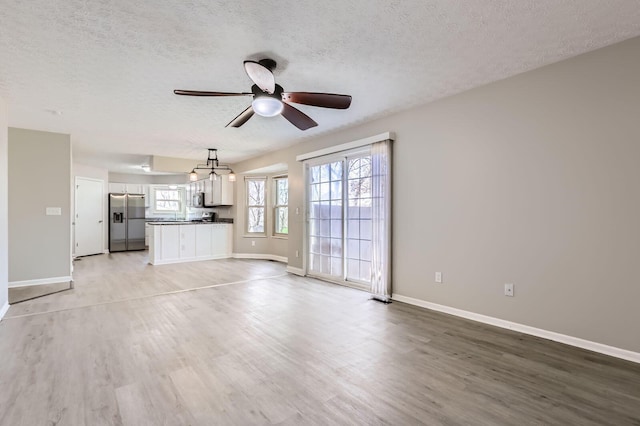 3225 Bellerive Dr, Pickerington, OH 43147 - unfurnished living room with light wood-style flooring, baseboards, a textured ceiling, and a ceiling fan