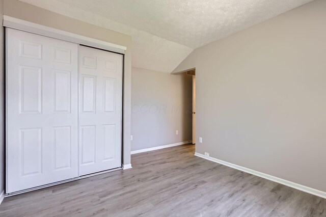3225 Bellerive Dr, Pickerington, OH 43147 - unfurnished bedroom featuring a closet, baseboards, vaulted ceiling, a textured ceiling, and light wood-style floors