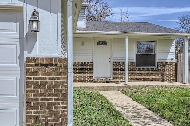 entrance to property featuring brick siding, a shingled roof, and covered porch